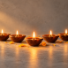 A neat row of small lit clay diyas on a stone surface, one diya slightly forward and glowing brighter, a few marigold petals scattered nearby